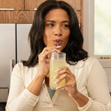 Woman drinking from a glass with a straw in a kitchen setting
