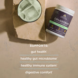 A tub of Ancient Nutrition Colostrum powder sits on a beige stone surface next to a glass of iced coffee on a piece of brown paper. Text below reads: 'SUPPORTS: gut health, healthy gut microbiome, healthy immune system, digestive comfort'.