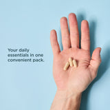 A human hand holding three beige capsules against a light blue background, with the text 'Your daily essentials in one convenient pack.' on the left.