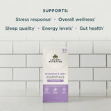 Ancient Nutrition Women's 40+ Essentials Vitality Pack box standing on a white surface against a white subway tile wall, with text above listing supported benefits including stress response, overall wellness, sleep quality, energy levels, and gut health.