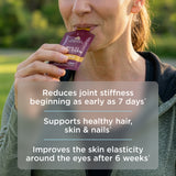 Person holding a supplement packet with text about its benefits on a blurred natural background