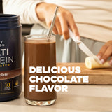 Glass of chocolate protein shake with a container of protein powder and a banana on a wooden cutting board.