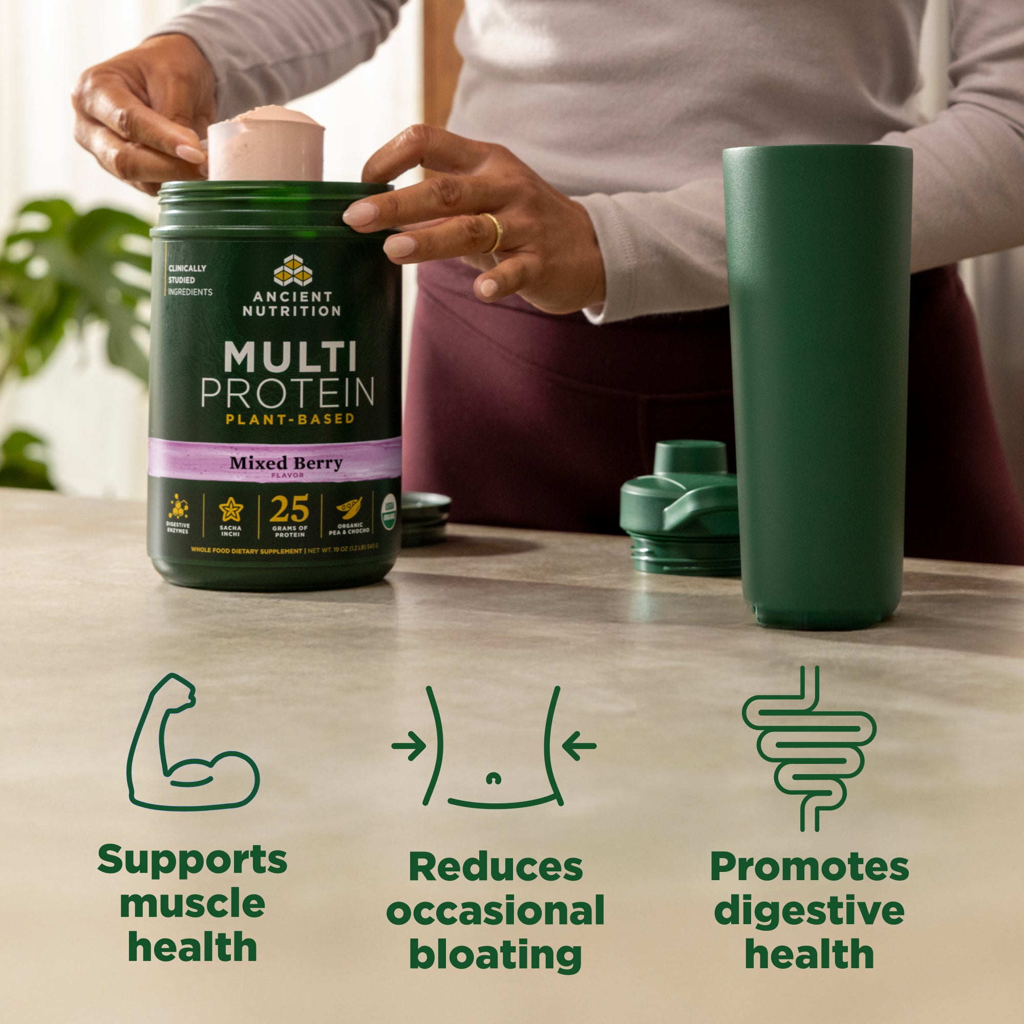 Person holding a container of Ancient Nutrition Multi Protein with a green tumbler on a table.