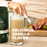 Glass of vanilla protein shake with a container labeled 'Protein' on a wooden surface.