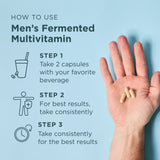 Hand holding capsules with instructions on how to use Men's Fermented Multivitamin on a light blue background