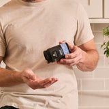 Person holding a supplement bottle with a neutral background