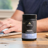 Ancient Nutrition Men's Multivitamin bottle on a table with a person using a laptop in the background