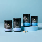 Four black supplement bottles from Ancient Nutrition arranged on a light blue studio background, with two beige capsules placed in front. The bottles are labeled Men's Once Daily Multivitamin, Men's Multivitamin, Men's Once Daily 40+, and Men's Once Daily with blue gradient label bands at the bottom.