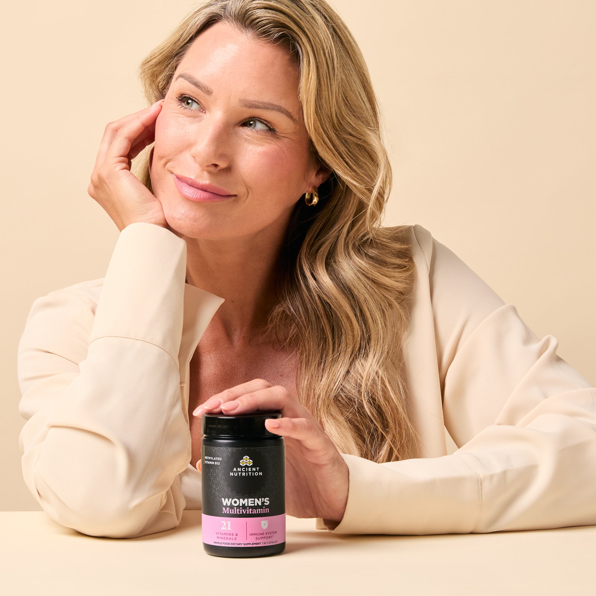 Woman holding a supplement bottle with a beige background