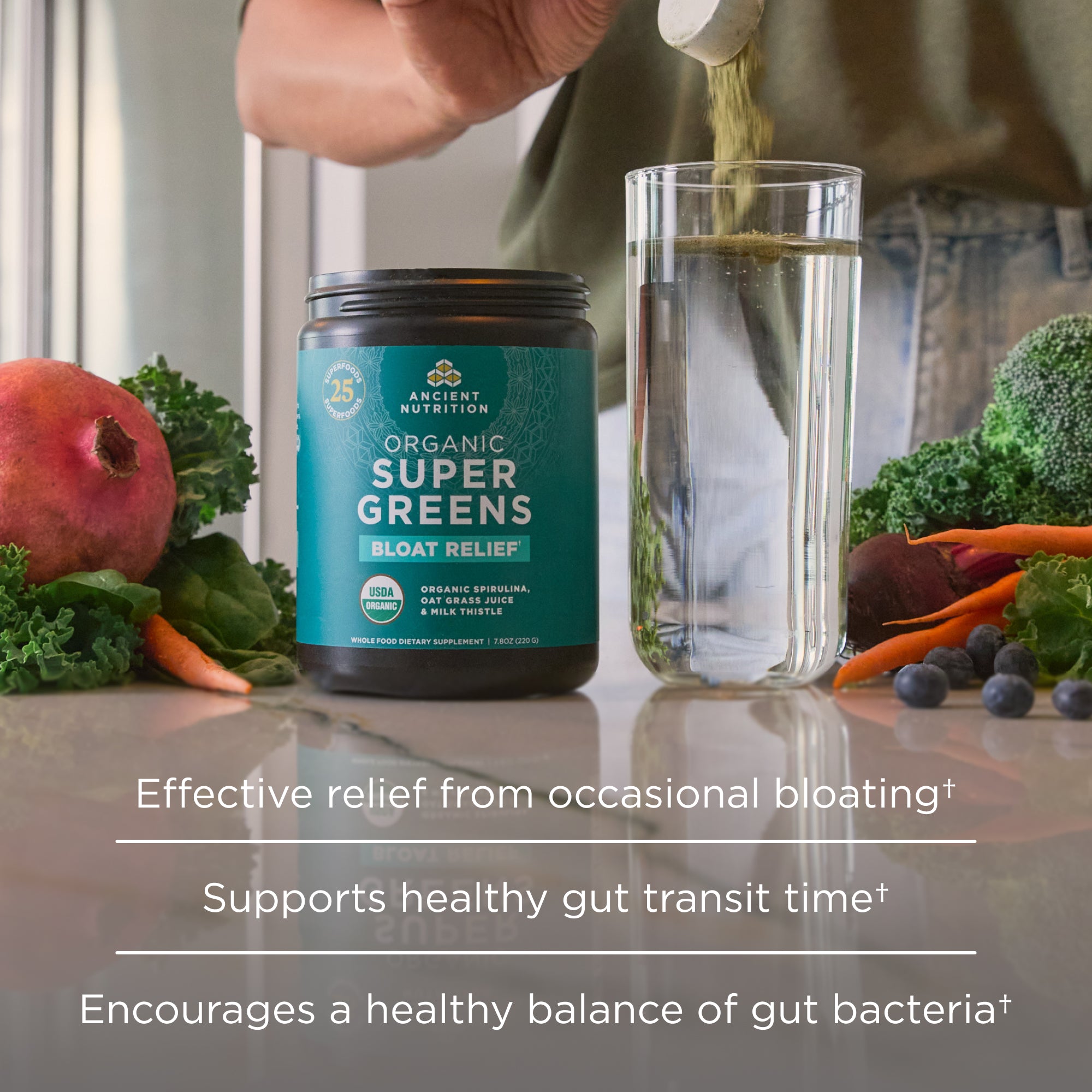 Bottle of Organic Super Greens with a glass of water and fresh vegetables on a table.