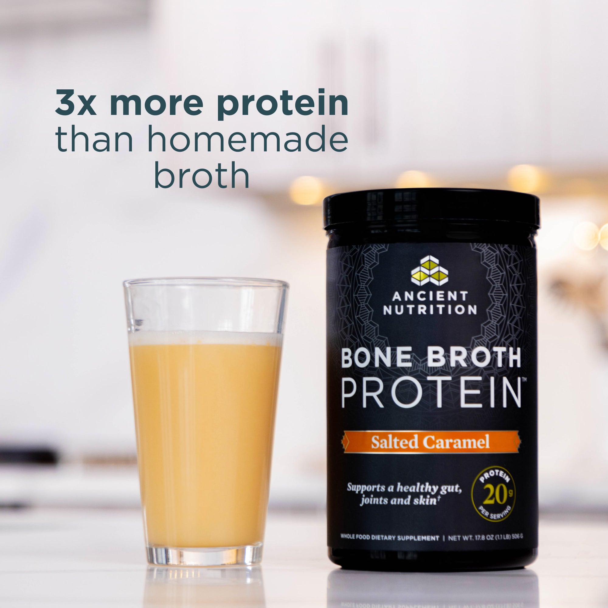 Ancient Nutrition Bone Broth Protein container with a glass of bone broth on a blurred background