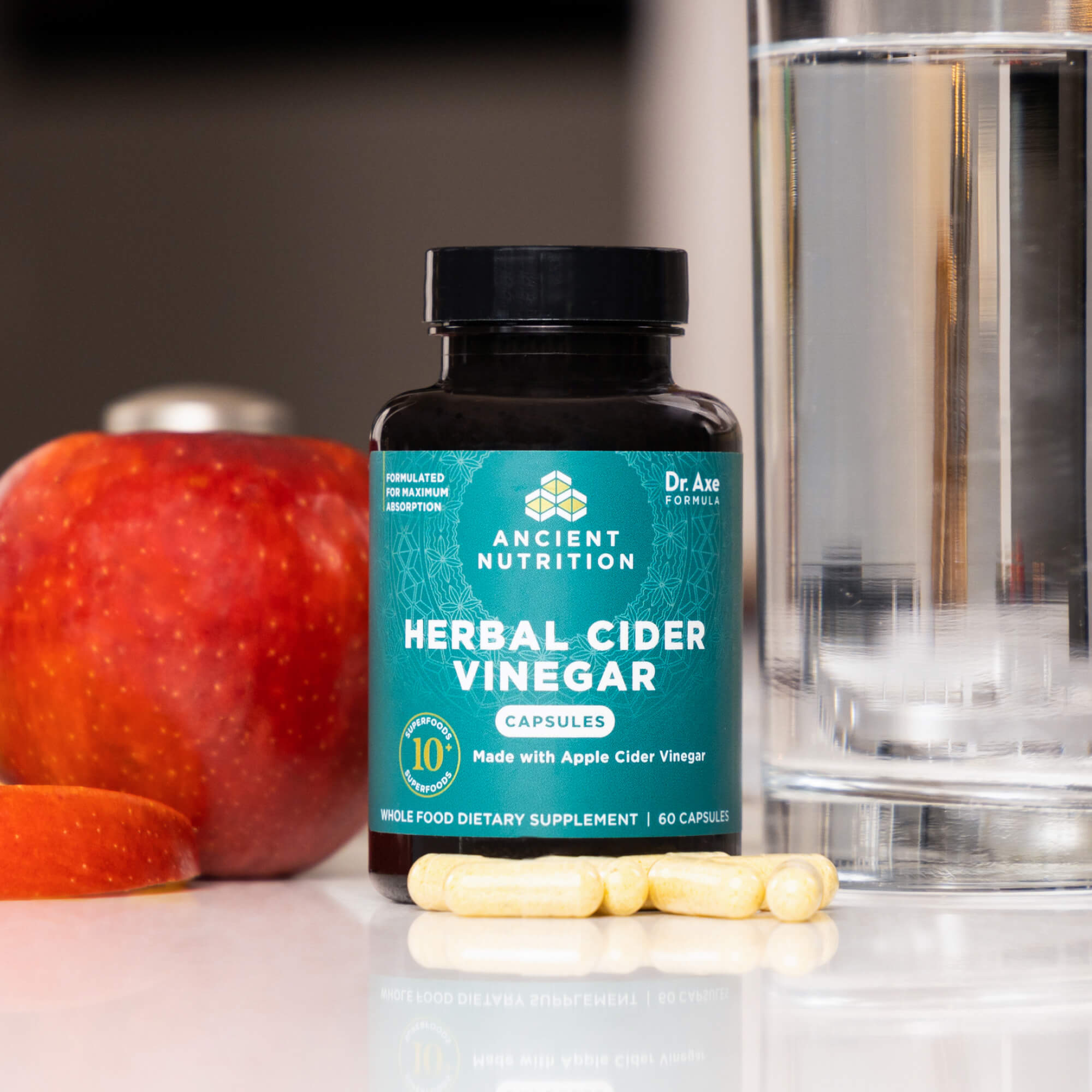 herbal cider vinegar capsules on a counter next to an apple
