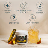 A jar of Organic Fiber supplement shown with a glass of orange drink, fruit slices, and feature callouts on a beige background.