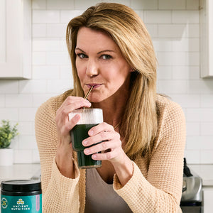 a woman drinking Organic SuperGreens Powder Berry Flavor (12 Servings)