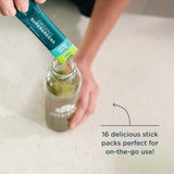 Person adding a SuperGreens stick pack into a glass bottle on a white surface.