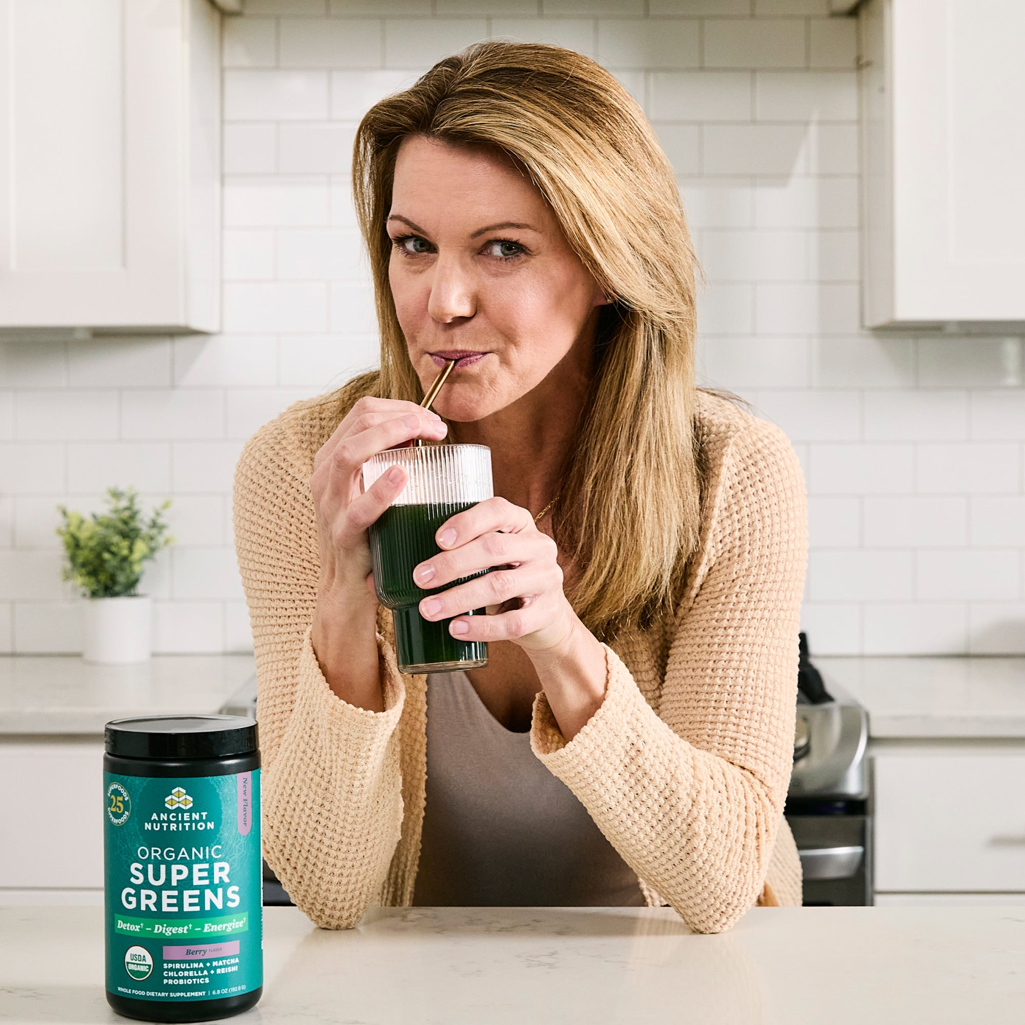 a woman drinking a glass of Organic SuperGreens Powder Berry Flavor (25 Servings)