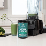 Ancient Nutrition Organic Super Greens container with a blender and glass of green juice on a kitchen counter.