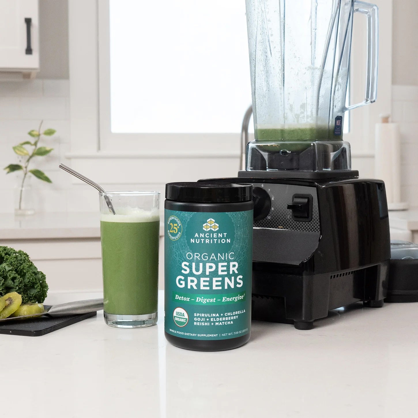 Ancient Nutrition Organic Super Greens container with a blender and glass of green juice on a kitchen counter.