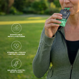 A woman outdoors on a grassy lawn holds a green and black supplement packet to her mouth. Three circular text callouts on the left describe product benefits: bioavailable, methylated forms; vitamin B12 + folate better together; balanced, easy-to-enjoy flavor.