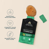 Ancient Nutrition Methylated Vitamin B12 in Passionfruit Lemonade flavor, shown as a black and green sachet with a green cap and a brownish-orange liquid droplet above it, on a beige background with three feature callouts on the left.