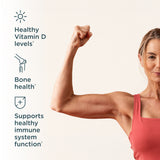 A woman in a coral pink tank top flexes her arm against a light beige background, with text on the left highlighting benefits: healthy Vitamin D levels, bone health, and support for healthy immune system function.