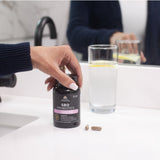 person grabbing a bottle of SBO Probiotics Women's Capsules from a bathroom counter