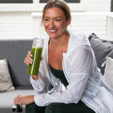 woman drinking a green juice on a couch 