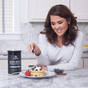 woman adding blueberries to a stack of pancakes